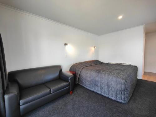 a bedroom with a bed and a leather couch at Camden Court Studio in Invercargill