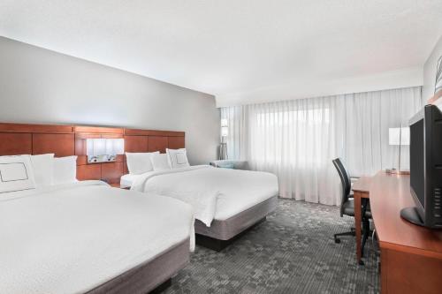 a hotel room with two beds and a desk and a tv at Courtyard Sarasota Bradenton Airport in Sarasota