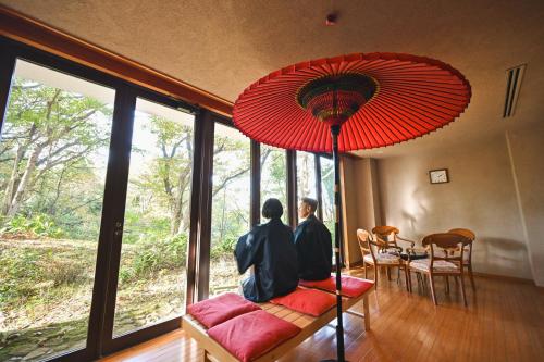 two people sitting on a bench under a red umbrella at 伊豆高原温泉ホテル 森の泉 in Ito