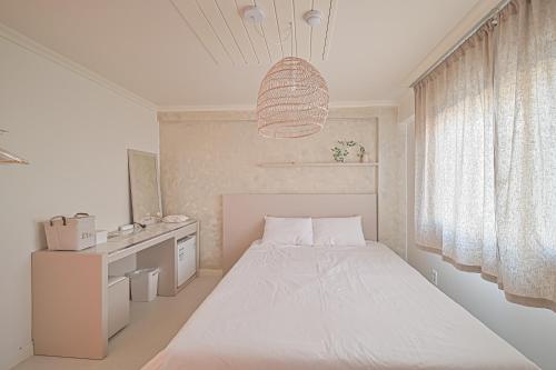 a white bedroom with a bed and a chandelier at In Stay Guesthouse in Seogwipo