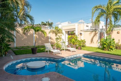 a swimming pool with chairs and a house at Casa privada con alberca grande in Chetumal