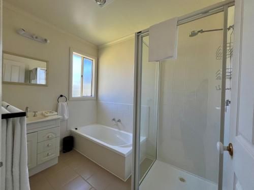 a bathroom with a shower and a tub and a sink at Promhills Cabins in Yanakie