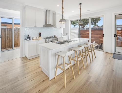 a kitchen with white cabinets and a kitchen island with bar stools at Banyandah on the Lakes in Paynesville