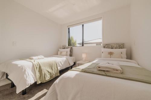 two beds in a white room with a window at Designer 2BR Flat - Outdoor Sitting & Cozy Ambiance in Christchurch