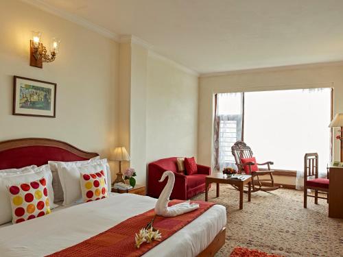 Club Mahindra Mashobra في ماشوبرا: غرفة بالفندق سرير وكرسي احمر