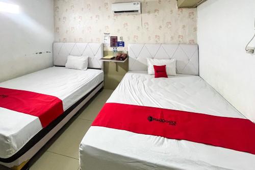 two beds in a room with red and white sheets at RedDoorz Syariah at Hostel Imah 3 Lampung in Kedaton