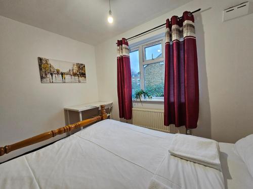 a bedroom with a bed with red curtains and a window at London E14 Rooms in London