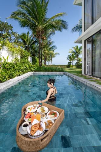 a child sitting in a pool with a tray of food at Wyndham Hoi An Royal Beachfront Resort & Villas in Hoi An