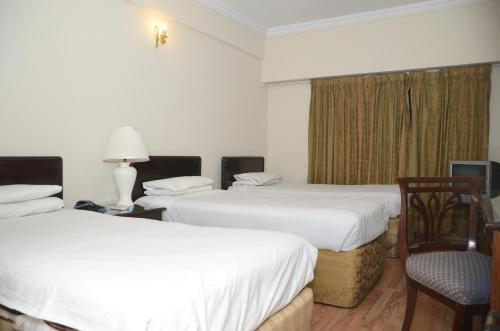 a hotel room with two beds and a chair at Carlton Tower Hotel Lahore in Lahore