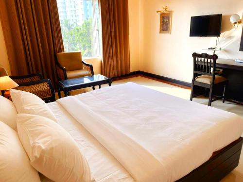 a bedroom with a large white bed with chairs and a desk at Hyson heritage calicut in Kozhikode