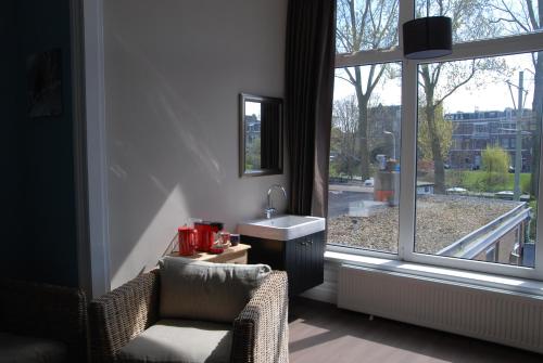 ein Badezimmer mit einem Waschbecken und einem Stuhl neben einem Fenster in der Unterkunft Bed & Breakfast Obrechtstraat in Den Haag