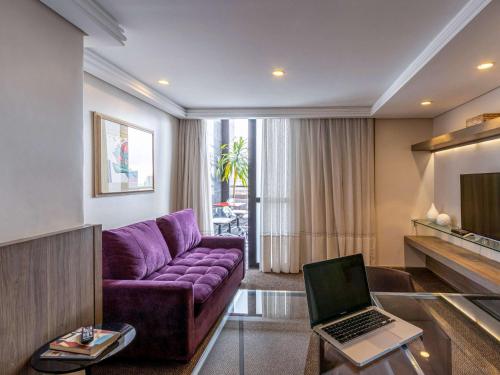 a living room with a purple couch and a laptop at Grand Mercure Curitiba Rayon in Curitiba