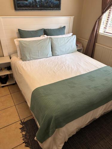 a bed with a green and white comforter and pillows at Garden View Seaside Chalet in Hibberdene