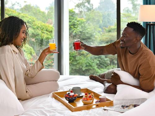 a man and a woman sitting in bed with drinks at Novotel Nairobi Westlands in Nairobi