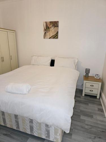 a bedroom with a large white bed and a night stand at Hollinwood Immaculate Home in Moston