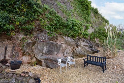 two chairs and a bench next to a rock wall at Luxury Holiday Apartments in Torquay