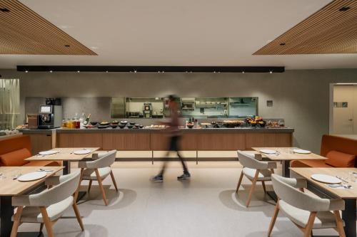 a woman walking through a restaurant with tables and a kitchen at Hotel Arconte, Adults Only in Barcelona