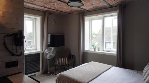 a bedroom with a bed and two windows and a fan at Boetiekhotel Ons Oude Raadhuis in Hooge Zwaluwe