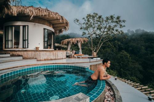 a man sitting in a swimming pool next to a house at Mountain Floating Cloud in Ban Kai Noi