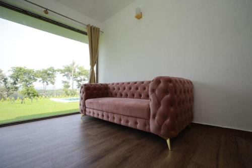 a brown couch in a room with a large window at The Winterfell Premium Homestay By Dazzle Destinations in Somvārpet