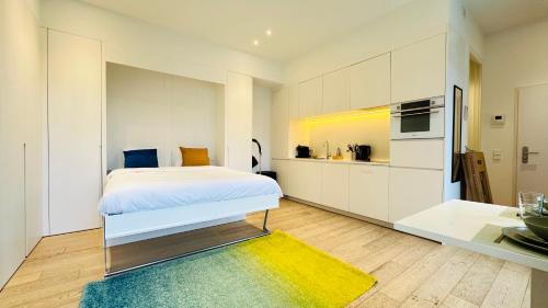 a white bedroom with a bed and a kitchen at Studio Fischer à la Pétrusse 002 in Luxembourg