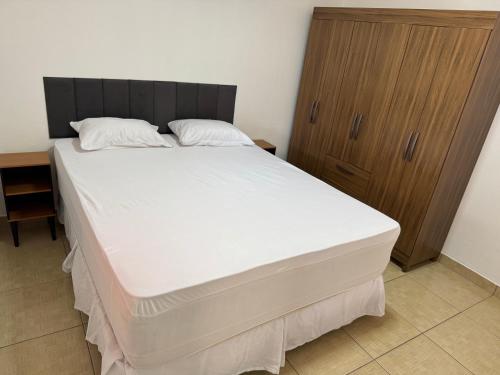 a bedroom with a large white bed with a wooden cabinet at Casa Aconchego Itaici in Caldas Novas