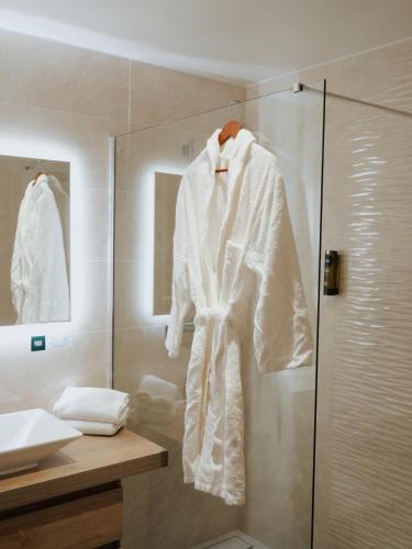La salle de bains est pourvue d'une douche et d'un peignoir blanc. dans l'établissement Logis Le Clos Deauville Saint Gatien, à Saint-Gatien-des-Bois
