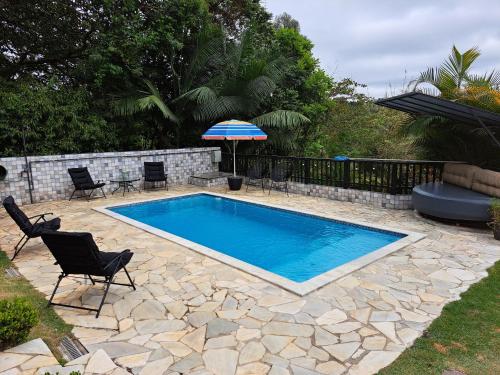 einen Pool mit Stühlen und einem Sonnenschirm in einem Hof in der Unterkunft Casa para relaxar, estilosa, privativa e pet friendly in Nazaré Paulista