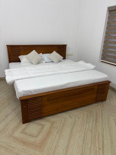 a large wooden bed with white sheets and pillows at Kannur Beachdrive Homestay in Thottada