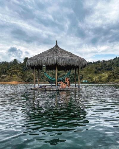 a woman laying in a hammock on a hut in the water at Levit Glamping - Hotel Guatapé Peñol in Guatapé