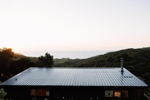 a house with a tin roof with the ocean in the background at Foudre Suite with Hot Tub at Barrelled Wines Raglan in Raglan