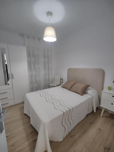 a white bedroom with a large bed and a lamp at Ático espacioso en zona céntrica in Sarria