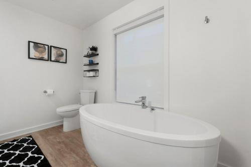 a white bathroom with a tub and a toilet at Central and Luxury 2BR Suite with Den & BBQ, Sleeps 6! in St. Catharines