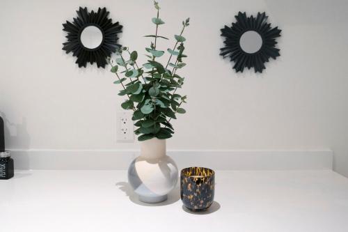 a white vase with a plant in it next to two mirrors at Central and Luxury 2BR Suite with Den & BBQ, Sleeps 6! in St. Catharines