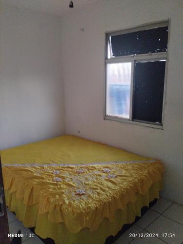 a bedroom with a bed with a yellow bedspread and a window at Cantinho da Dete in Salvador