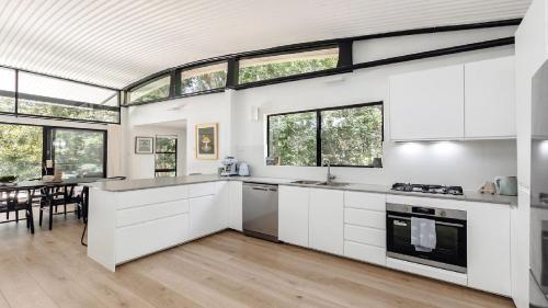 una cocina abierta con armarios blancos y ventanas en Elegant Abode Only Moments To Macmasters Beach, en Macmasters Beach