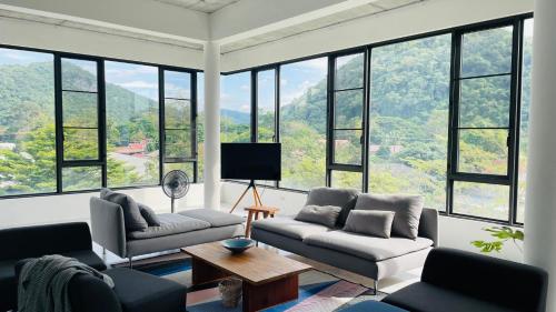 a living room with a couch and a tv and windows at ATATvilla Khaoyai with mountain rooftop view for party and BBQ in Mu Si