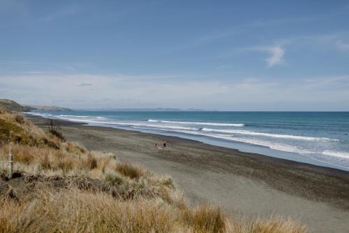 a beach with a person on the sand and the ocean at Barrique Studio with Sauna at Barrelled Wines Raglan in Raglan