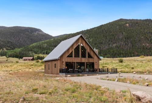 a large wooden barn in a field with mountains at BHA - Luxury A-Frame in Creede
