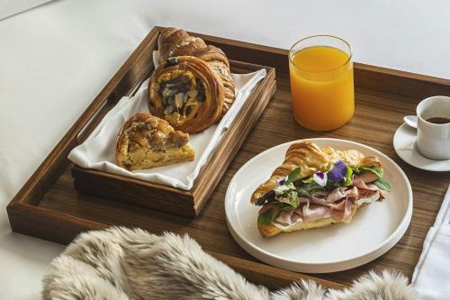 ein Tablett mit einem Sandwich und einem Teller mit Brot und Orangensaft in der Unterkunft The Rome EDITION in Rom