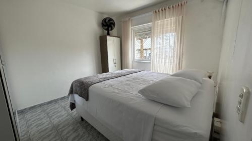 a bedroom with a white bed and a window at Aconchegante apartamento 2 dormitórios no centro com vaga in Capão da Canoa