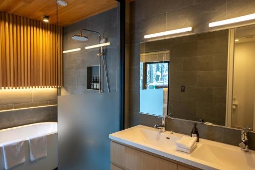 a bathroom with a sink and a tub and a mirror at Koyo Onsen Chalet in Niseko
