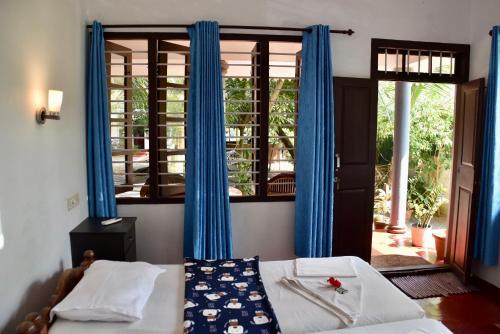 a bedroom with a bed and a window with blue curtains at Marari Beach Villas in Mararikulam