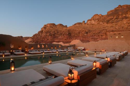 a resort pool with lounge chairs and a mountain at Dar Tantora The House Hotel in AlUla