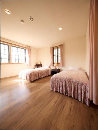 two beds in a room with wooden floors and windows at カナリアンホテル in Tateshina