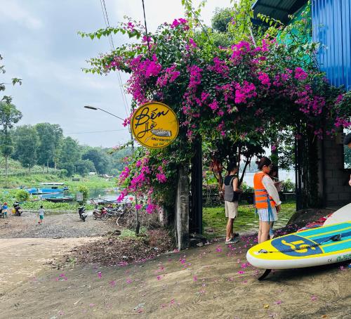 a man standing next to a building with flowers and a surfboard at Bến Hồ Homestay in Xã Gia Tân