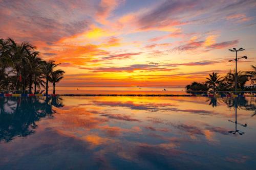 a sunset over a swimming pool with palm trees at Langco Bay Retreat in Lang Co