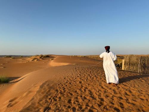 a man standing in the sand in the desert at Desert Moments Camp in Al Wāşil