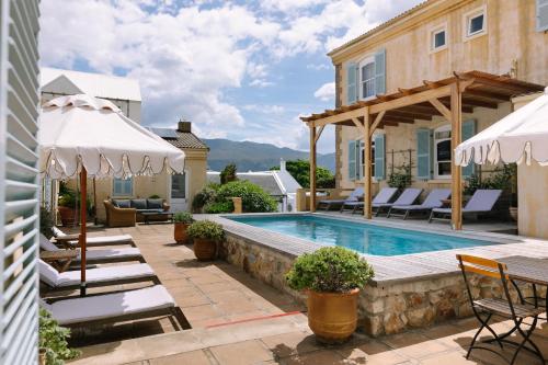 a pool with chairs and umbrellas next to a house at Auberge Burgundy Boutique Hotel & Spa in Hermanus