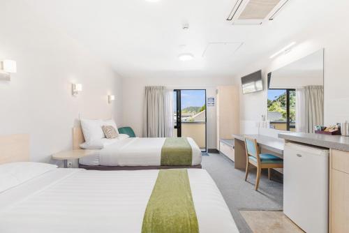 a hotel room with two beds and a desk at Bella Vista Motel Whangarei in Whangarei